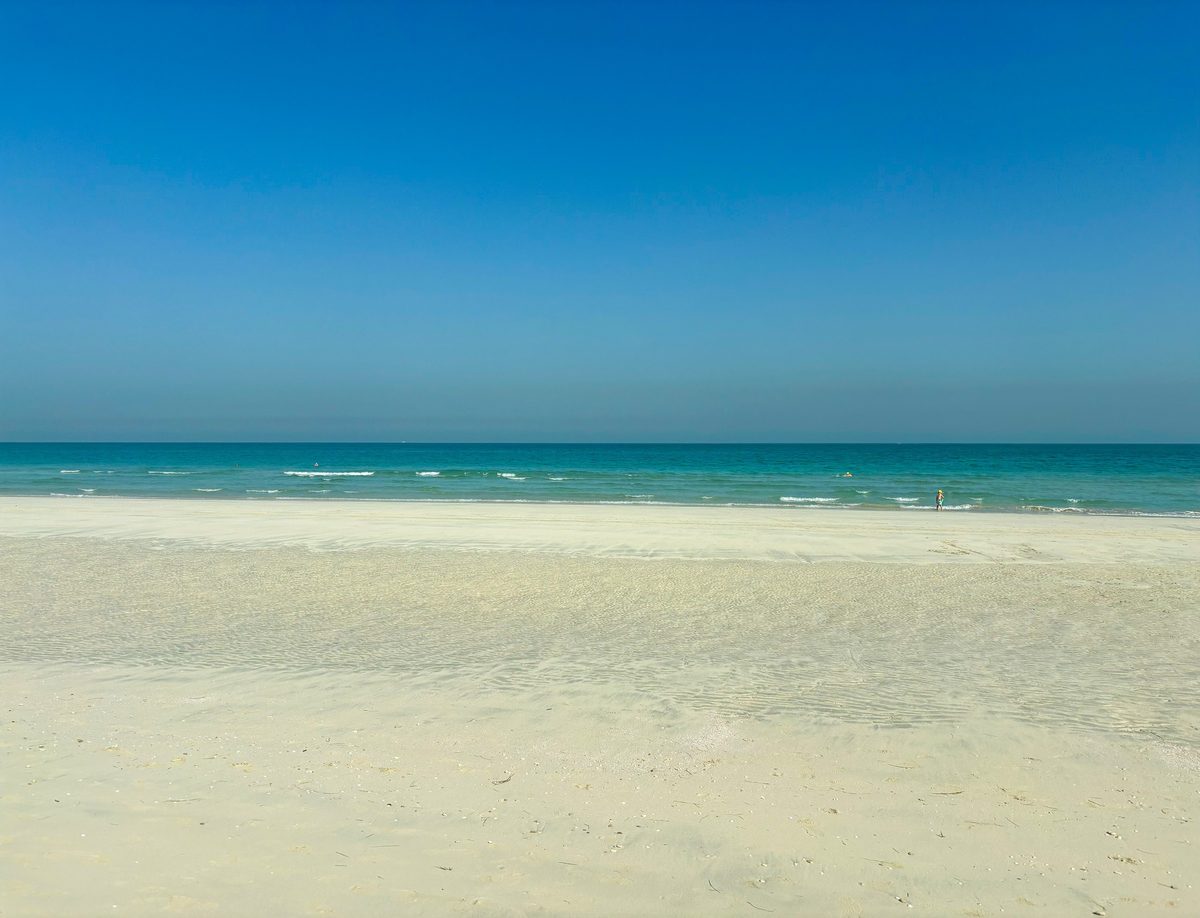 An empty Saadiyat beach in the morning: pale sand, a band of turquoise, then the deep blue of the open Gulf