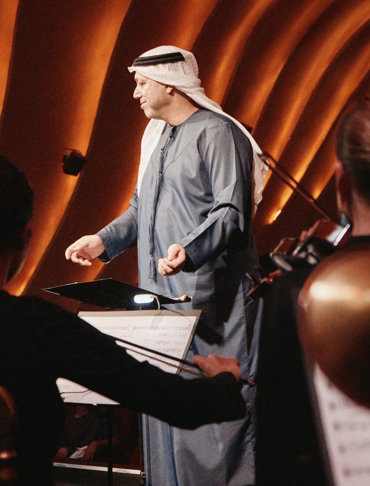 A conductor in a kandura leading an orchestra on stage