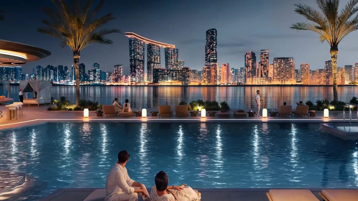 A pool at night with loungers and lanterns, the lit city skyline across the water