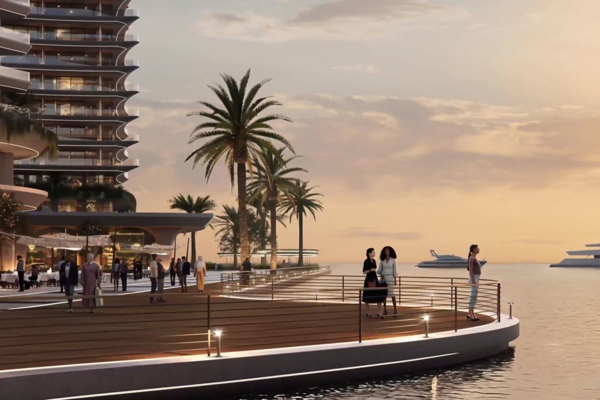 La promenade de la marina au crépuscule : un platelage bois incurvé le long de l'eau, des palmiers, une tour résidentielle au-dessus de la colonnade commerçante et des yachts amarrés au loin