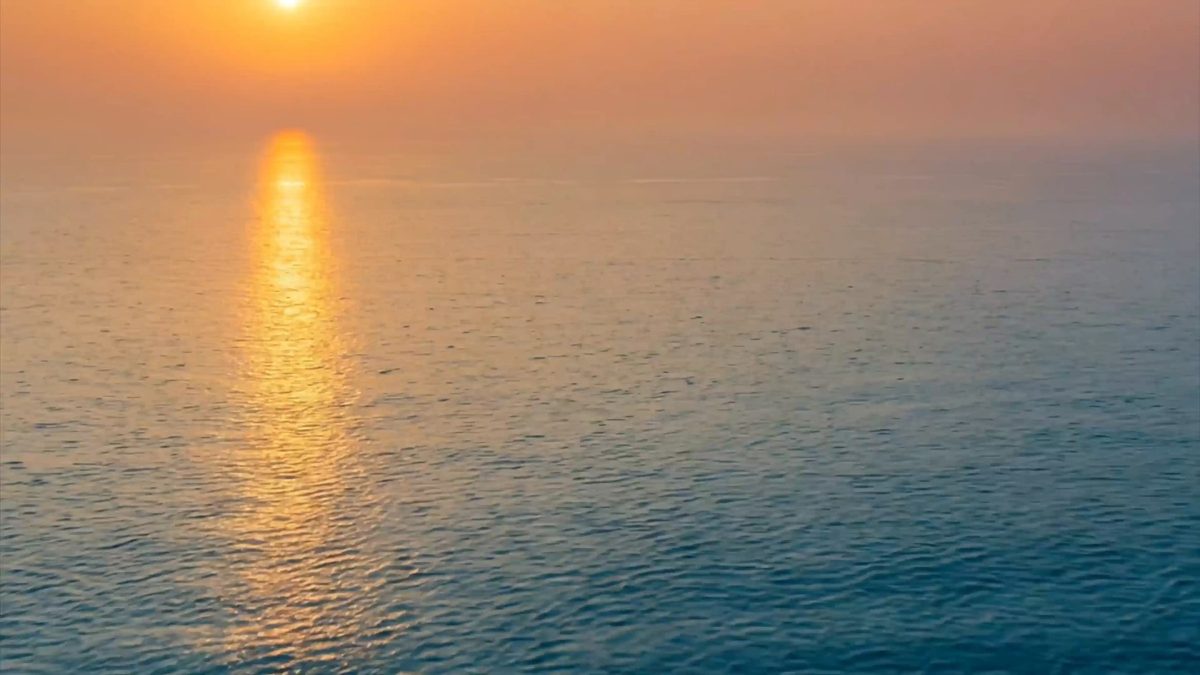 Die tief stehende Sonne über einem ruhigen, offenen Meer, ihr Spiegelbild zeichnet einen hellen Pfad auf dem Wasser