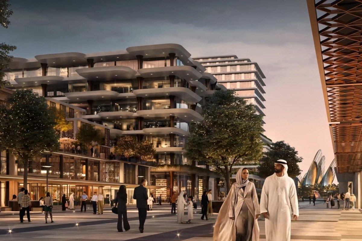 Un immeuble résidentiel aux balcons arrondis au-dessus d'une colonnade commerçante éclairée au crépuscule, des passants sur la promenade
